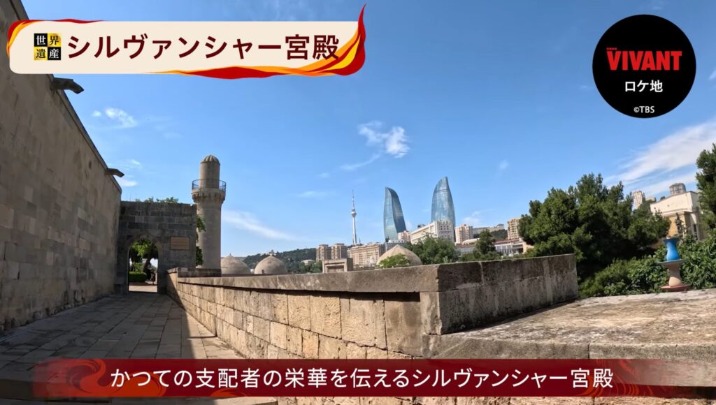 画面左上に「世界遺産 シルヴァンシャー宮殿」、右上に「VIVANT ロケ地 ©TBS」、下部に「かつての支配者の栄華を伝えるシルヴァンシャー宮殿」とテロップが入った番組の紹介画面。手前には歴史ある石造りの宮殿や細い塔(ミナレット)が写り、澄み渡る青空の背景には、炎のような形をした近代的な高層ビル「フレームタワー」が佇んでいる。古代の歴史遺産と現代の都市景観が融合した、アゼルバイジャン・バクーの風景。