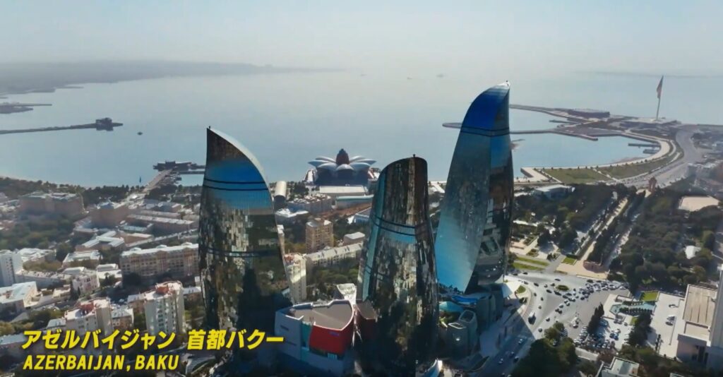 アゼルバイジャンの首都バクーの海岸沿いに建つ、炎の形をした3棟の巨大な高層ビル「フレイム・タワーズ」の空撮画像です。左下には「アゼルバイジャン 首都バクー」という字幕が配置されています。
