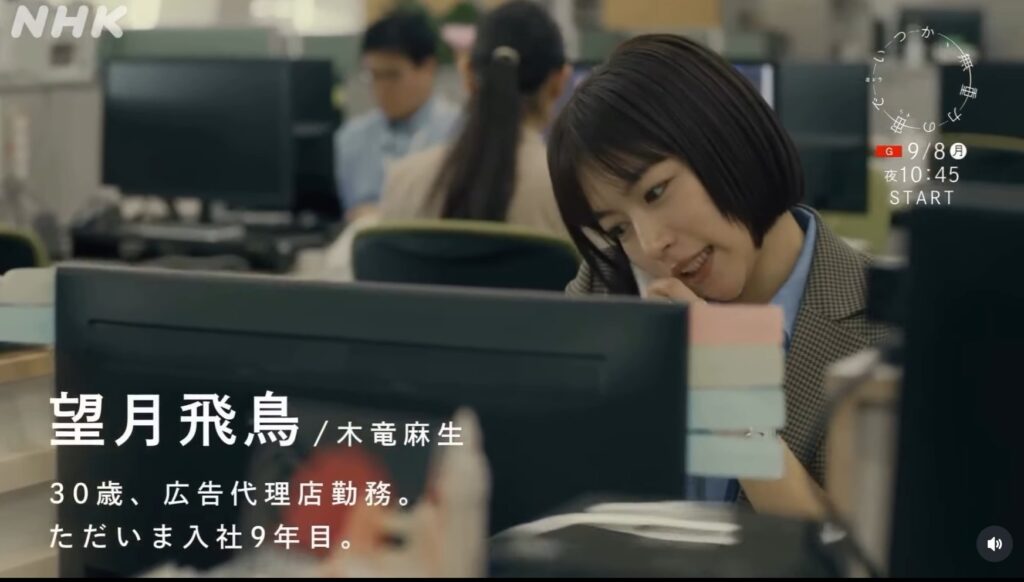 ドラマいつか、無重力の宙でのシーン。オフィスでPCに向かう望月飛鳥役の木竜麻生。彼女は茶色のジャケット姿で、真剣な表情をしている。画面には望月飛鳥/木竜麻生 30歳、広告代理店勤務 入社9年目の紹介テキストが表示されている。