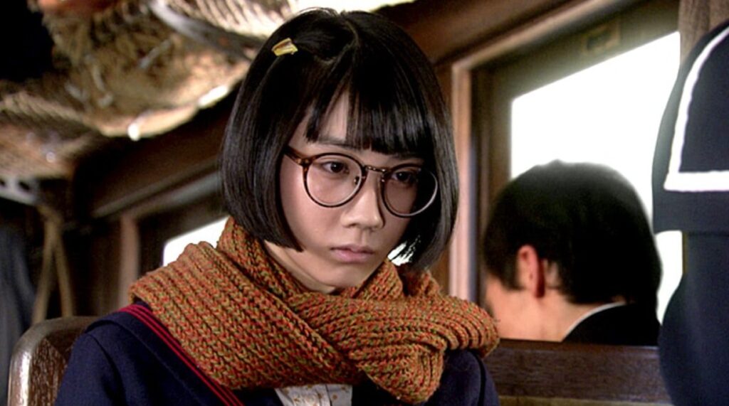 朝ドラ『ひよっこ』で青天目澄子を演じる松本穂香さんのワンシーン。丸眼鏡をかけ、オレンジ色のマフラーを巻いたセーラー服姿で、憂いのある表情で何かを考えている様子。古い日本家屋の室内が背景。
