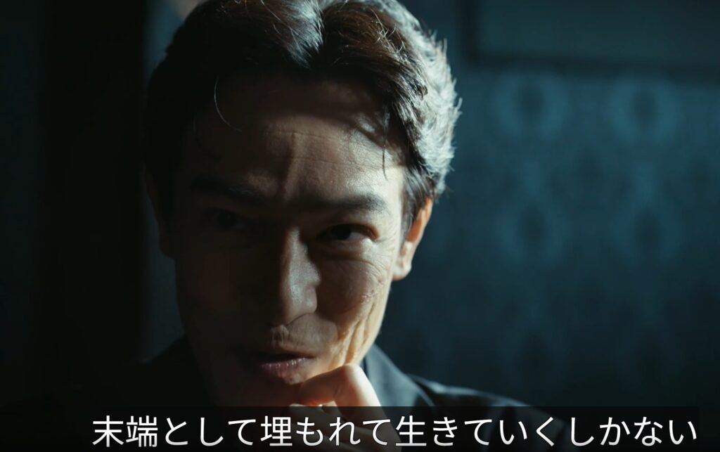 ドラマ『VIVANT』第19話のワンシーンです。暗い背景の中、顔の片側に深い影を落としたリュウ・ミンシュエンが、険しい視線で前方を見つめています。画面下部には「末端として埋もれて生きていくしかない」という白い字幕が表示されています。