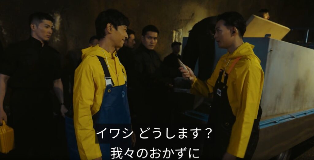 ドラマ『VIVANT』第19話、暗いトンネルで黄色い作業着姿の新庄が数匹のイワシを手に乃木に「イワシ どうします?」と尋ねるシーン。乃木の返答は字幕で「我々のおかずに」。周囲には他の作業員の姿がある。