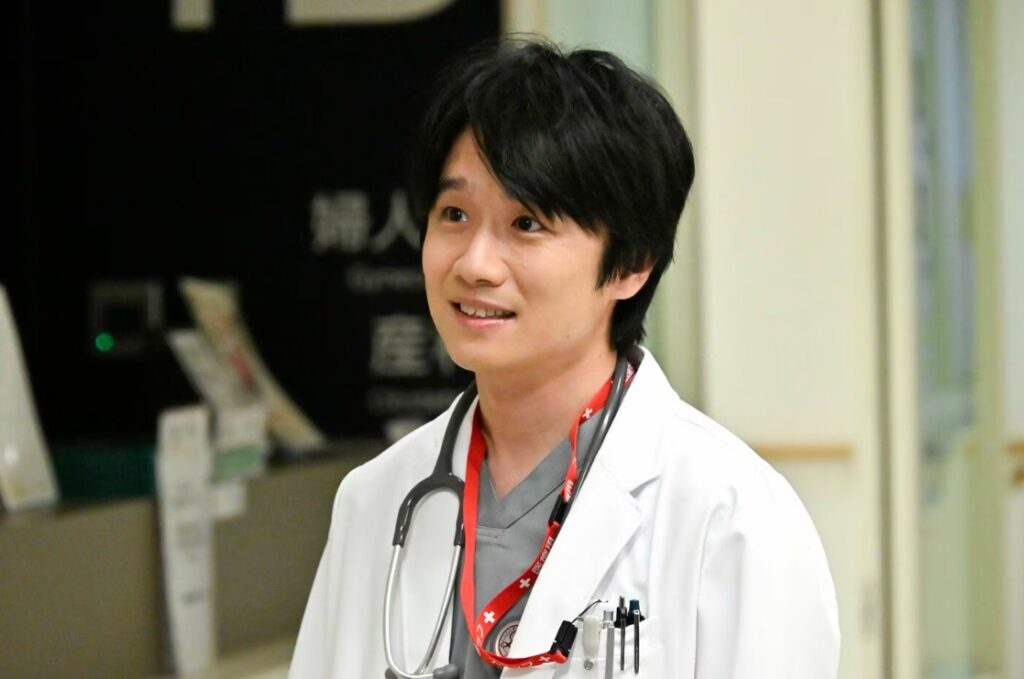 テレビドラマ『救命病棟24時』のワンシーン。俳優の風間俊介さんが演じる広瀬斎が、白衣を着用して首に聴診器を下げた状態で、病院内の廊下に立ち、柔らかく優しい表情でどこかを見つめながら会話している様子です。