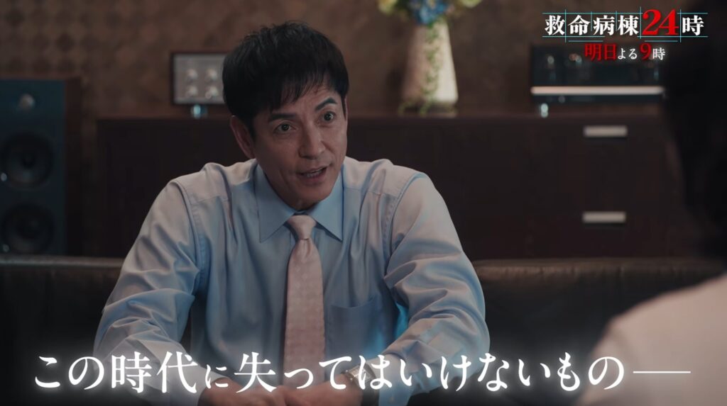『救命病棟24時』新シリーズのワンシーン。水色のワイシャツとピンクのネクタイ姿でソファに座る落合雅人（沢村一樹さん）が話す様子。画面上部に番組ロゴと「明日よる9時」、下部に「この時代に失ってはいけないもの――」のテロップ。