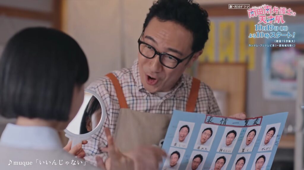 ドラマ『南田南弁護士は天才肌』のワンシーン。エプロン姿の角田晃広さんが、驚いた表情で手鏡と「表情一覧表」のフリップを子供に見せている。鏡には角田さんの顔が映り、フリップには様々な表情の写真が並ぶ。右上にはドラマロゴと告知のテロップ。