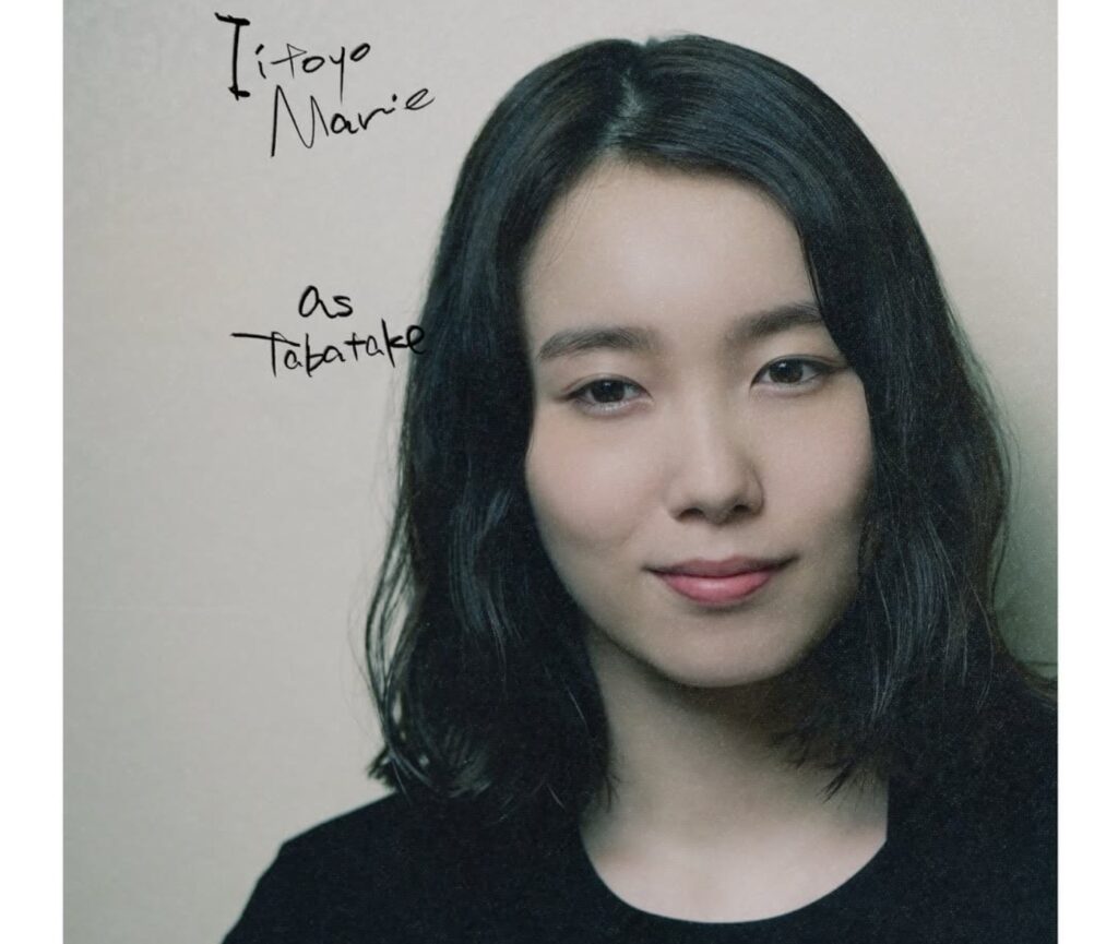『LOST10』で田畠役を演じる飯豊まりえさんのポートレート。黒髪のミディアムヘアに黒い服装で、カメラに向かって優しく微笑んでいます。画像の上部には、手書き風の英語で「Itoyo Marie」と記載されています。