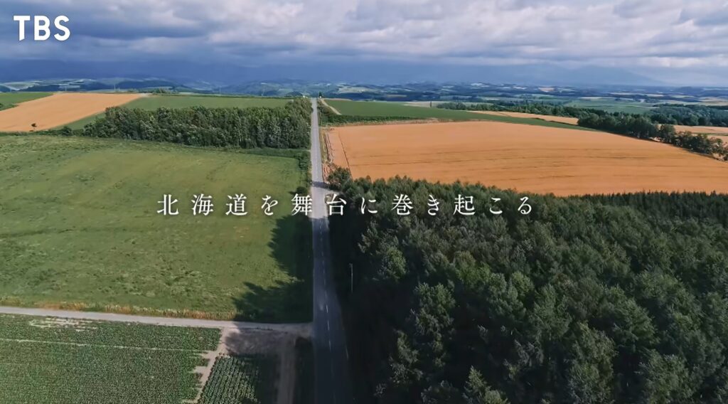 TBSの番組『LOST10(ロストテン)』のワンシーン。北海道の広大な畑や深い森の中を、遠くへと一直線に伸びるアスファルトの道路を上空から捉えた空撮映像。画面の中央には「北海道を舞台に巻き起こる」という白い字幕が表示されている。