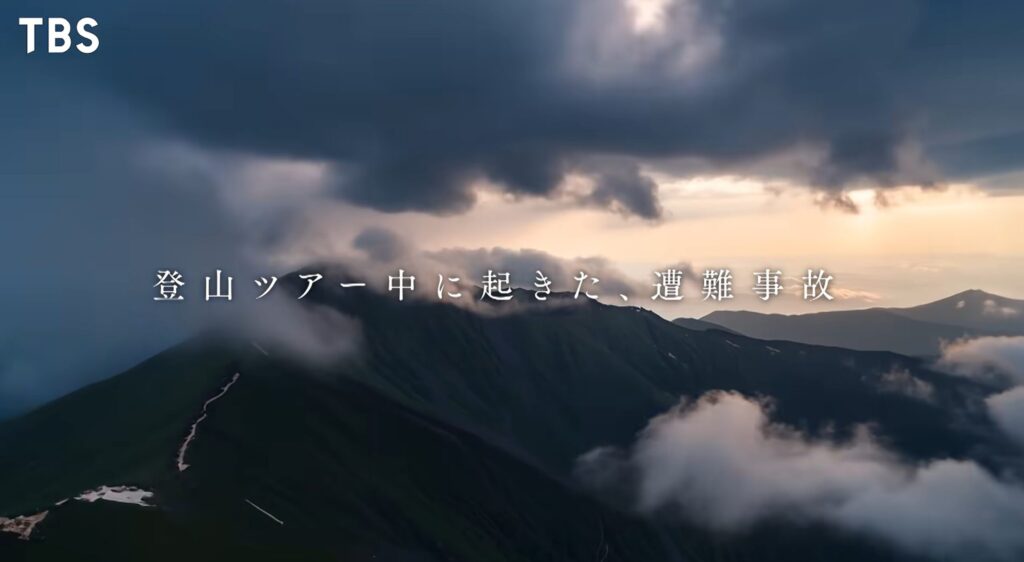TBS『LOST10(ロストテン)』の映像。厚い雲の下、残雪のある暗く険しい山脈を捉えた空撮。画面中央には、白いフォントで「登山ツアー中に起きた、遭難事故」と書かれたテロップが表示されている。