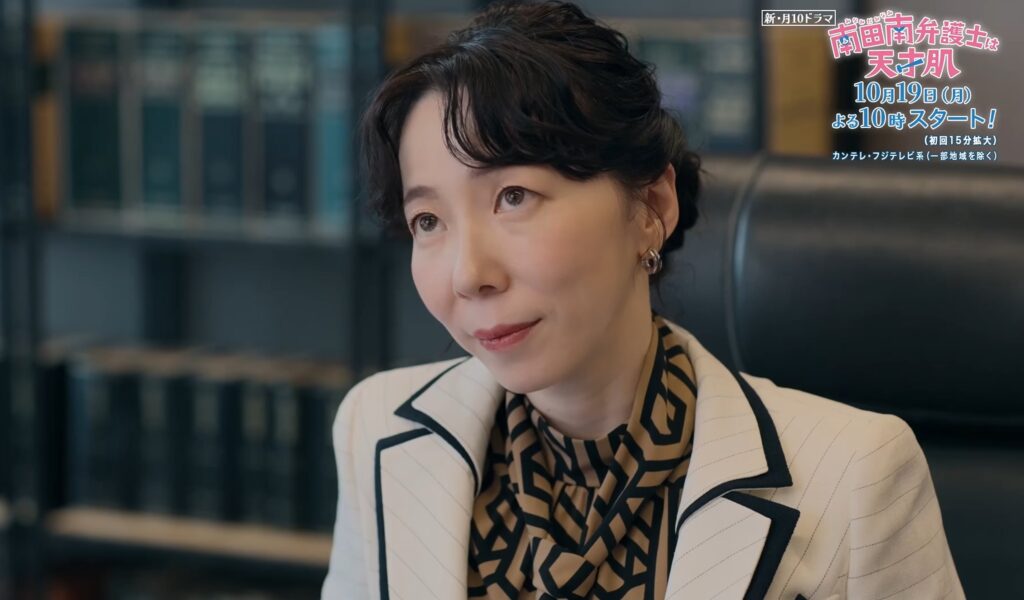 法律事務所のような場所で、女性が物思いにふけりながら上を見上げる。白のパイピングブレザーと幾何学模様のインナーを着用。右上には新ドラマ「南田南弁護士は天才肌」のロゴ。