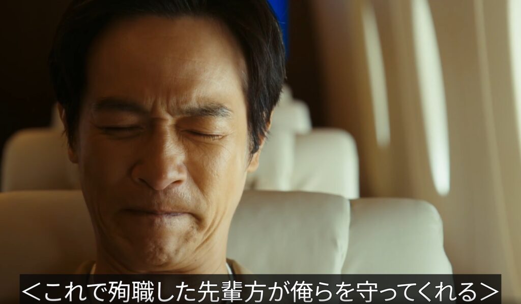 ドラマ『VIVANT』のワンシーン。飛行機の座席に座り、目を固く閉じて厳しい表情で何かを噛み締める乃木憂助のアップ。画面下部には「これで殉職した先輩方が俺らを守ってくれる」という字幕が黒い帯の上に白文字で表示されている。
