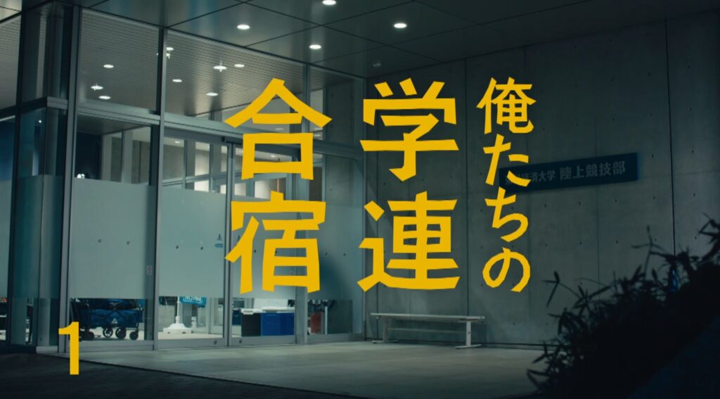 夜間の近代的な大学施設の外観。ガラス張りの自動ドアやコンクリートの壁が広がるエントランスに、黄色い大きな文字で『俺たちの学連合宿』と作品タイトルが重なっている。