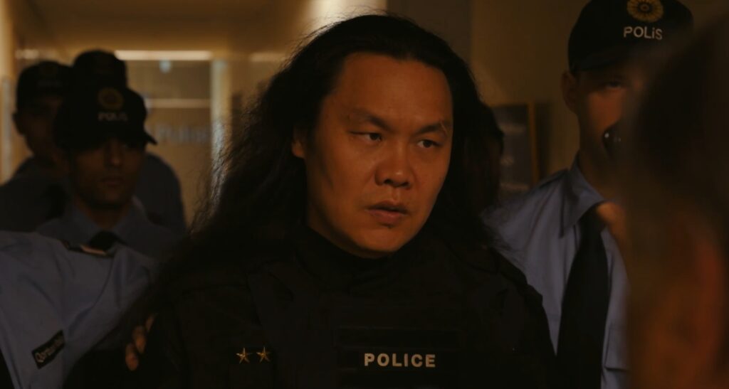『VIVANT』第22話のワンシーン。ゴルバド警察に捕まったチンギスが、警察官たちに周囲を取り囲まれながら険しい表情で連行されている場面。