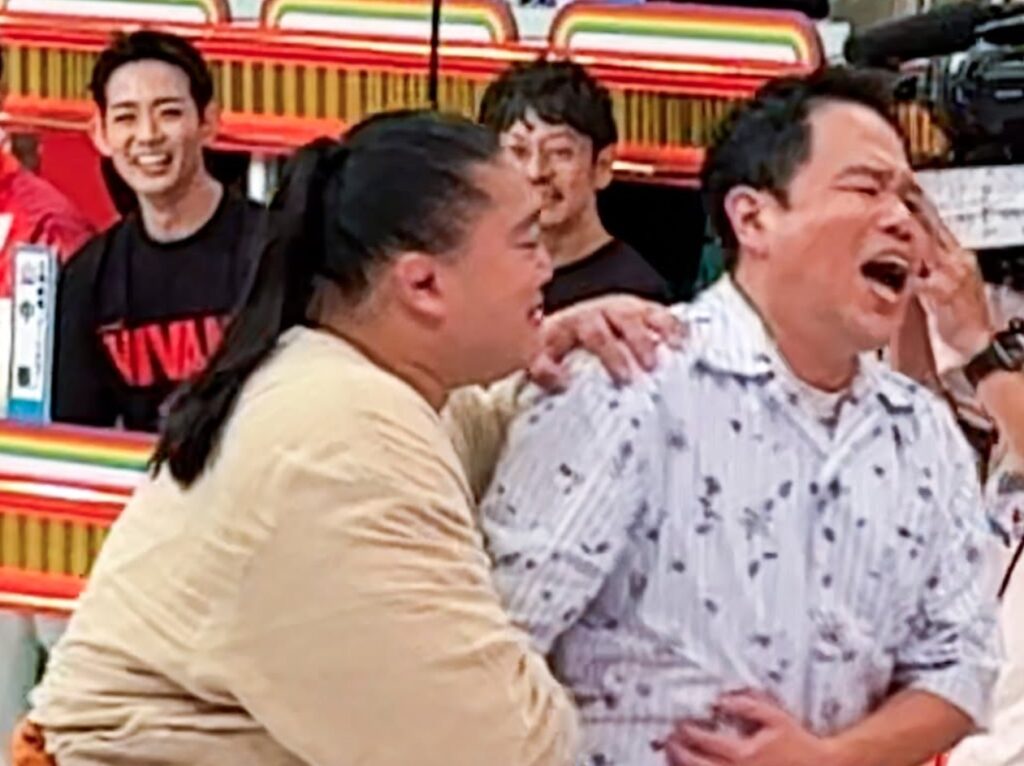 『オールスター感謝祭』のスタジオで、ドラムさんに抱きつかれて肩をつかまれ、口を大きく開けて大声で叫ぶような表情を見せるダイアンの津田篤宏さん。後ろでは出演者が笑顔で見守るにぎやかなワンシーン。