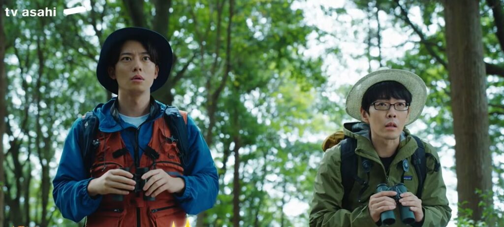 『アナログナース』第2話のワンシーン。緑豊かな森の中で、双眼鏡を手にした動物言語学者の鈴木俊貴さんと、内科医・羽鳥哲生役の井上祐貴さんが、驚いた表情で遠くを見つめている様子。
