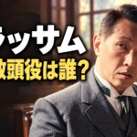 朝ドラ『ブラッサム』の上野教頭をイメージした横長イラスト。灰色のスーツ姿の男性を右側に大きく描き、木造の職員室と明るい窓を背景にしています。左側には「ブラッサム」「上野教頭役は誰?」の文字を白と黄色で配置しています。